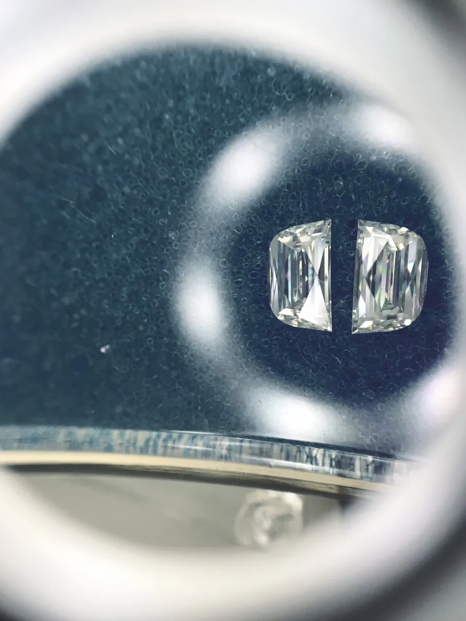 Two matched half-moon diamonds viewed through a jeweller's loupe.