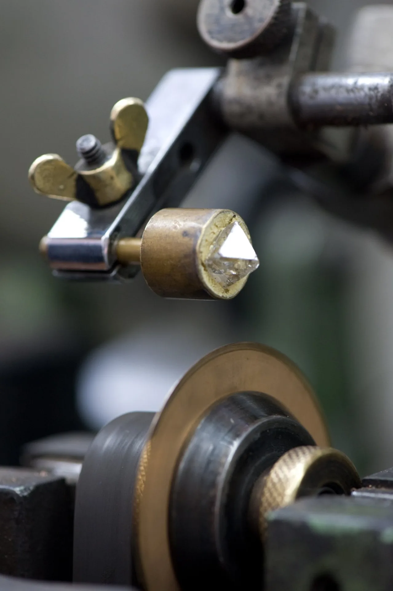 A rough diamond held on a dop above a traditional polishing wheel.